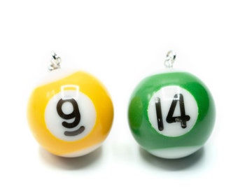 May include: Two spherical charms shaped like billiard balls. The left charm is yellow and white with the black number 9, and the right charm is green and white with the black number 14. Each charm features a small silver metal jump ring at the top.