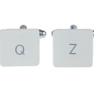 May include: A pair of white cufflinks with silver accents. The cufflinks are shaped like computer keys, one with the letter "Q" and the other with the letter "Z".