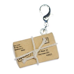 Könnte beinhalten: Ein kleines braunes Papierpaket, das mit Schnur zusammengebunden ist und einen silbernen Schlüsselanhänger hat. Das Paket hat einen "FRAGILE"-Stempel und Adressen für "75 Oak Ave, Smalltown, CA 98447" und "23 Main St, Tinytown, OH 43521".