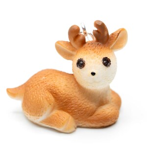 Könnte beinhalten: Eine kleine, braune Keramik-Hirschfigur mit großen, braunen Augen. Der Hirsch sitzt mit leicht geneigtem Kopf.