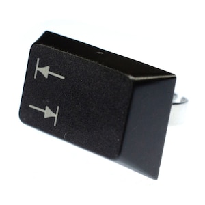 Peut inclure: Touche de clavier noire en plastique avec deux flèches blanches pointant vers le haut et vers le bas. La touche est fixée à un support métallique argenté.