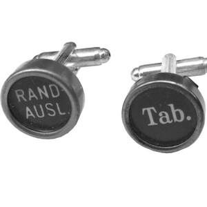 May include: A pair of cufflinks made from vintage typewriter keys. One cufflink features the text "RAND AUSL." and the other cufflink features the text "Tab."