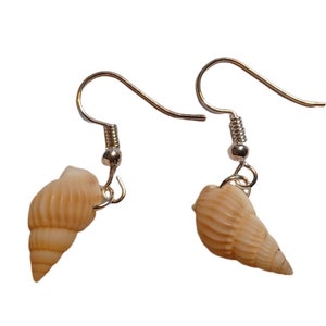 Peut inclure: Une paire de boucles d'oreilles en argent avec un charme en forme de coquillage. Les coquillages sont de couleur beige clair.