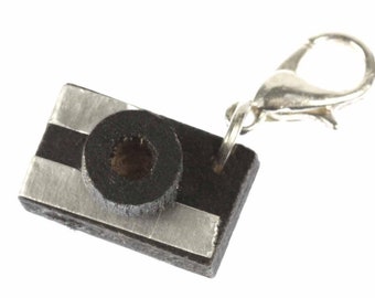 May include: A small wooden camera charm with a black and silver design and a silver metal clasp.
