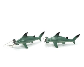 May include: A pair of green hammerhead shark earrings. The sharks are made of plastic and have silver hooks.