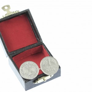 May include: Two silver German 1 Deutsche Mark coins in a black velvet box with a red interior. The box has a small silver latch.