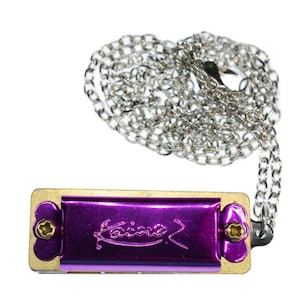 May include: A purple harmonica with a silver chain attached. The harmonica has the word "Kaina" written on it.