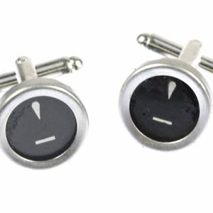 May include: A pair of silver cufflinks with black and white typewriter keys. The keys feature the exclamation point and the underscore.