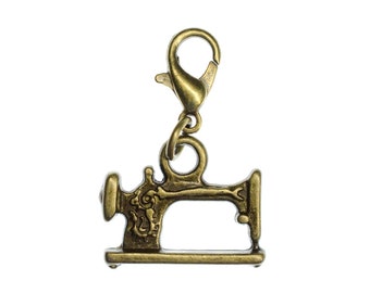 Pode incluir: Um amuleto de máquina de costura de metal dourado com um fecho de lagosta. O amuleto é detalhado com um design decorativo no lado da máquina de costura.
