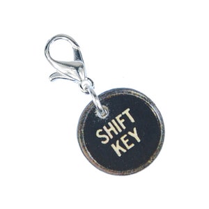 May include: A black and silver key chain charm with a round black tag that says "SHIFT KEY" in white lettering.