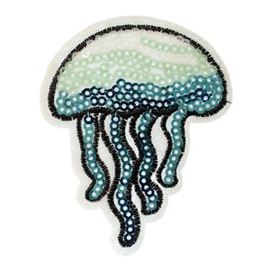 Peut inclure: Un patch en forme de méduse en sequins bleus et verts. La méduse est bordée de fil noir et a un fond blanc.