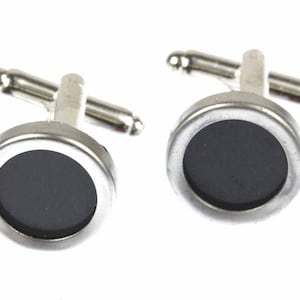 May include: A pair of silver cufflinks with black circular insets.