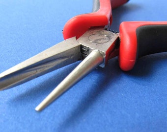 May include: Close-up of a pair of red and black pliers with a long, pointed nose. The pliers are made of metal and have a black rubber grip.