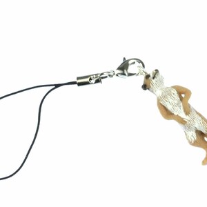 May include: A brown and white meerkat figurine attached to a black phone charm string with a silver clasp.