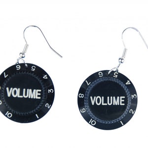 May include: A pair of black volume knob earrings with silver hooks. The knobs have white numbers from 1 to 10 and the word "VOLUME" printed on them.