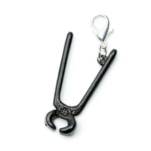 May include: Black metal pliers with a silver metal clasp. The pliers are a keychain charm.