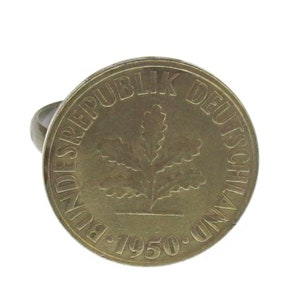 Può includere: Un anello dorato con un design a forma di moneta. La moneta presenta una foglia di quercia e il testo "BUNDESREPUBLIK DEUTSCHLAND 1950".