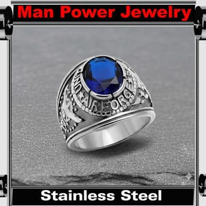 May include: A stainless steel ring with a large, round, blue gemstone at the center. The ring is engraved with the words "United Air Force" and other details. The text "Man Power Jewelry" and "Stainless Steel" are displayed.
