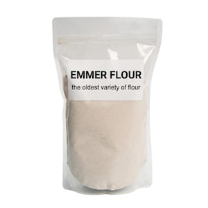 May include: A clear, resealable plastic pouch filled with off-white emmer flour. A white rectangular label on the front features the black text EMMER FLOUR and the smaller text the oldest variety of flour, centered on the bag against the powder.