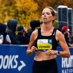 以下が含まれることがあります： 白いナイキのロゴが入った黒いスポーツタンクトップを着たランナー。ゼッケンには「STEPHANIE」、番号「156」、年号「2022」が記載されている。ランナーは左手首に白いデジタルスポーツウォッチを着用して走っている。