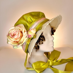 Può includere: Un cappello in stile vintage nei toni del verde, crema e rosa, adornato da una grande rosa e piccoli boccioli. Il cappello presenta un'ampia tesa, un nastro di raso e un grande fiocco. Il cappello è esposto su una testa di manichino.