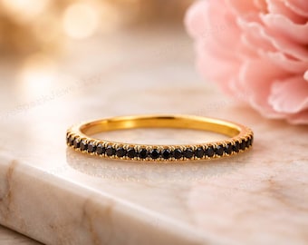 May include: A thin gold band ring featuring a continuous row of small, round, faceted black stones set along the entire circumference. The metal has a polished finish, and the stones are uniform in size, creating a sleek, circular design.