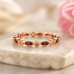 Könnte beinhalten: Ein Ewigkeitsring aus Roségold mit einem abwechselnden Muster aus tiefroten Steinen im Marquise-Schliff und gelben Steinen im Rundschliff, die in einem durchgehenden Band gefasst sind. Das Metall hat ein poliertes Finish und ein sich wiederholendes Muster.