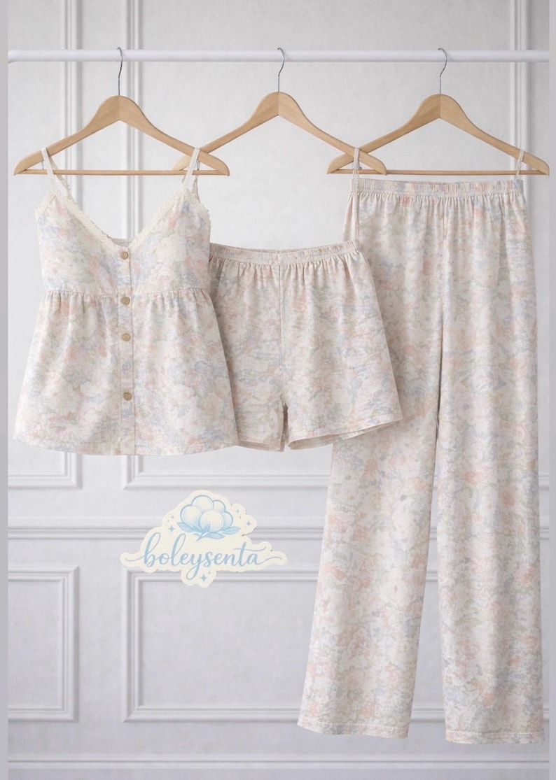 May include: A three-piece pajama set with a floral pattern in soft pastel colors. The set includes a camisole top with lace trim, button details, shorts, and long pants, all hanging on wooden hangers.