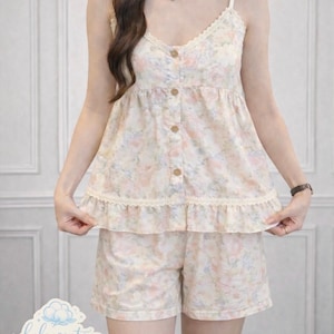 May include: A two-piece pajama set featuring a floral pattern in pastel colors. The top has a camisole style with lace trim and wooden buttons. The shorts have a matching floral print and a ruffled hem. The brand name "boleysenta" is visible.