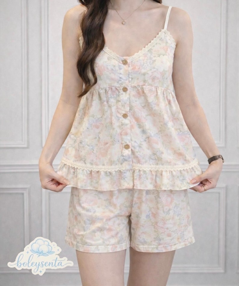 May include: A two-piece pajama set featuring a floral pattern in pastel colors. The top has a camisole style with lace trim and wooden buttons. The shorts have a matching floral print and a ruffled hem. The brand name "boleysenta" is visible.