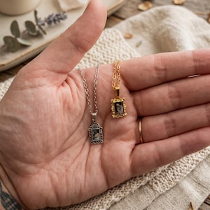 May include: Two rectangular pendant necklaces, one in silver-tone metal and one in gold-tone metal. Each pendant features an ornate, filigree-style frame surrounding a small, central portrait image. Both pendants hang from matching delicate link chains.