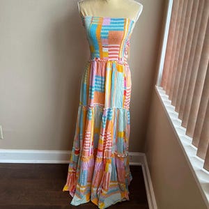 May include: A strapless maxi dress in a patchwork design. The dress features a mix of colors including blue, orange, pink, and yellow. The bodice is smocked, and the skirt has tiered ruffles. The dress is displayed on a mannequin.