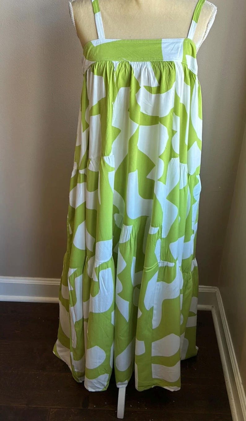 May include: A floor-length, sleeveless dress with a white and lime green abstract pattern. The dress features a square neckline and wide straps. The fabric is lightweight and flowy, with tiered ruffles at the skirt.