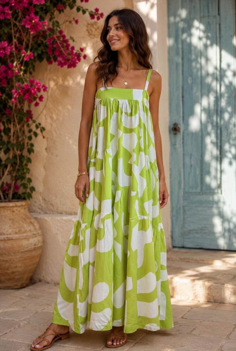 May include: A long, flowing dress in a vibrant lime green and white abstract pattern. The dress features a square neckline, wide straps, and a tiered skirt. The model is wearing brown sandals and a gold necklace.