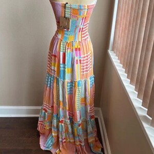 Pode incluir: Vestido maxi sem al&ccedil;as com um design de patchwork em cores vibrantes. O vestido apresenta um corpete justo e uma saia esvoa&ccedil;ante. As cores incluem rosa, laranja, azul e amarelo. Uma etiqueta est&aacute; presa ao vestido.