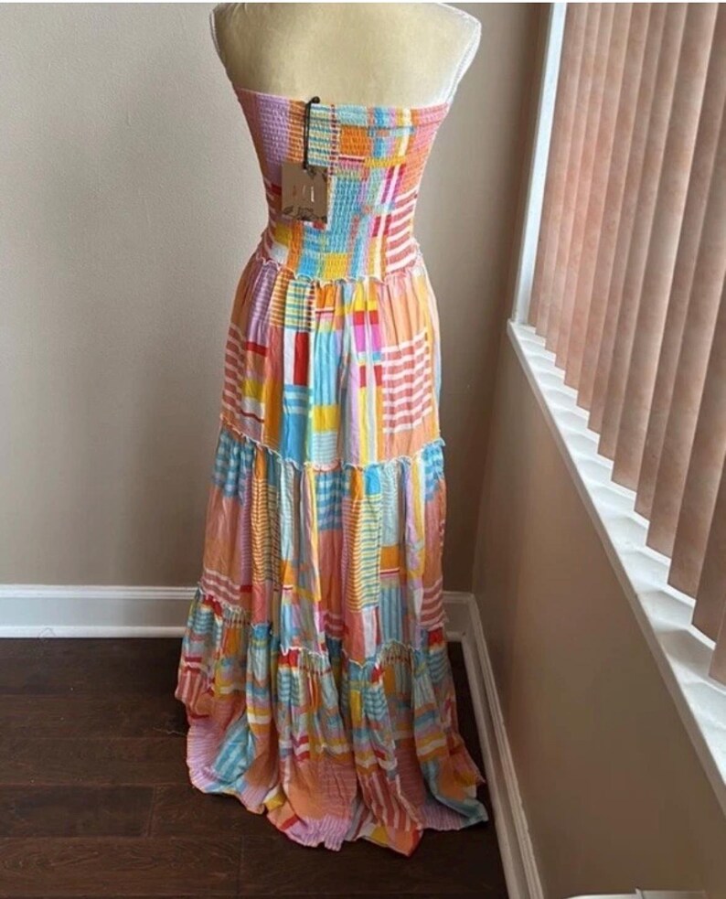 Pode incluir: Vestido maxi sem al&ccedil;as com um design de patchwork em cores vibrantes. O vestido apresenta um corpete justo e uma saia esvoa&ccedil;ante. As cores incluem rosa, laranja, azul e amarelo. Uma etiqueta est&aacute; presa ao vestido.