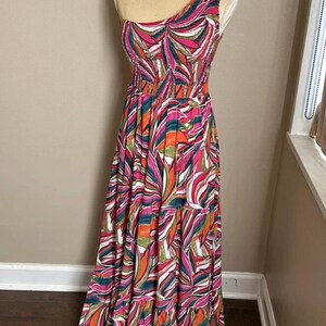 May include: A colorful, one-shoulder maxi dress with a vibrant leaf-like pattern in shades of pink, orange, green, and white. The dress features a fitted bodice and a flowing, tiered skirt, perfect for warm weather.