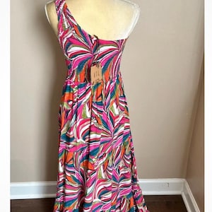 May include: A colorful, one-shoulder maxi dress with a vibrant abstract pattern in pink, orange, green, and white. The dress features a fitted bodice and a flowing skirt. A tag with the letters "ITL" is attached.