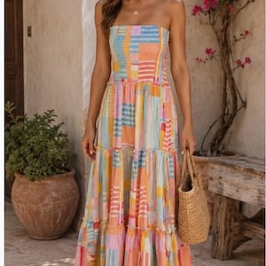 Pode incluir: Um vestido longo sem al&ccedil;as com um design de patchwork em cores pastel. O vestido apresenta um corpete ajustado e uma saia em camadas. A mulher est&aacute; carregando uma bolsa de m&atilde;o tecida. O fundo inclui um vaso de terracota com uma planta e um banco de madeira.