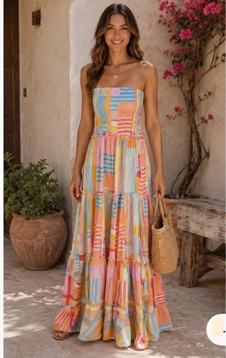 Pode incluir: Um vestido longo sem al&ccedil;as com um design de patchwork em cores pastel. O vestido apresenta um corpete ajustado e uma saia em camadas. A mulher est&aacute; carregando uma bolsa de m&atilde;o tecida. O fundo inclui um vaso de terracota com uma planta e um banco de madeira.