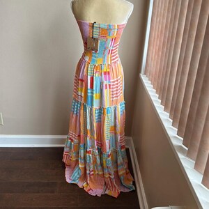 May include: A colorful strapless maxi dress with a patchwork design. The dress features a mix of orange, pink, blue, and yellow rectangular patterns. The dress has a tiered skirt and is displayed on a mannequin.