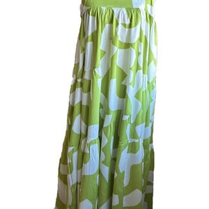 May include: A sleeveless, tiered dress in a vibrant green and white abstract pattern. The dress features wide shoulder straps and a flowing, relaxed fit. The fabric appears lightweight, suitable for warm weather.