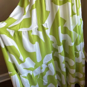 May include: A flowing, tiered dress in white and lime green. The dress features a bold, abstract pattern of lime green shapes against a white background. The fabric appears lightweight and suitable for warm weather.