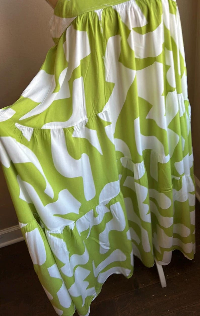 May include: A flowing, tiered dress in white and lime green. The dress features a bold, abstract pattern of lime green shapes against a white background. The fabric appears lightweight and suitable for warm weather.