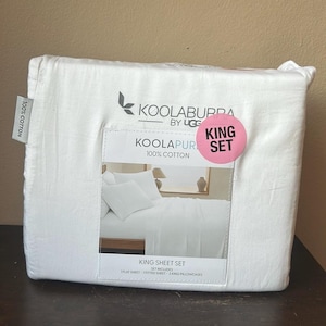 May include: A white King sheet set, packaged and sealed. The packaging features the brand name "KOOLABURRA by UGG" and the text "KOOLAPUR 100% COTTON". A pink sticker reads "KING SET". The set includes a flat sheet, fitted sheet, and two king pillowcases.