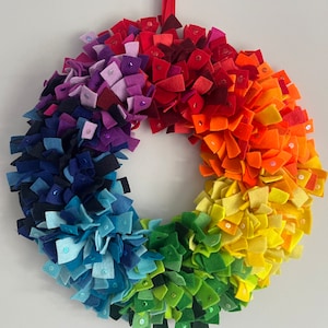 May include: A rainbow felt wreath with sequins. The wreath is made of felt squares in shades of red, orange, yellow, green, blue, indigo, and violet.