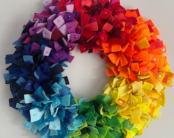 May include: A rainbow felt wreath with sequins. The wreath is made of felt squares in shades of red, orange, yellow, green, blue, indigo, and violet.