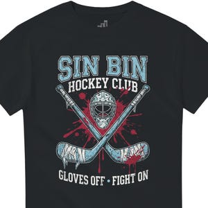 May include: Black t-shirt with a hockey-themed graphic. The design features crossed hockey sticks, a goalie mask, and the text "SIN BIN HOCKEY CLUB" in light blue. The phrase "GLOVES OFF - FIGHT ON" is also included.