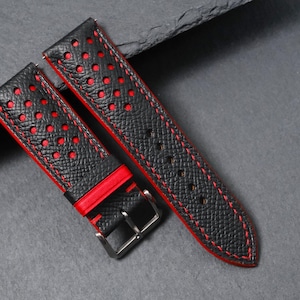 May include: Black watch strap with red accents. The strap features a textured surface with red stitching and perforated holes. The edges are trimmed in red, and the buckle is silver.
