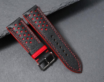 May include: Black watch strap with red detailing. The strap has a textured finish, red stitching, and perforated holes. The edges are red, and the buckle is silver.